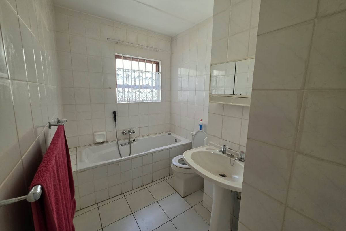 A functional bathroom featuring a pedestal basin, built-in bathtub with shower mixer, and tiled finishes throughout, offering potential for modernization.