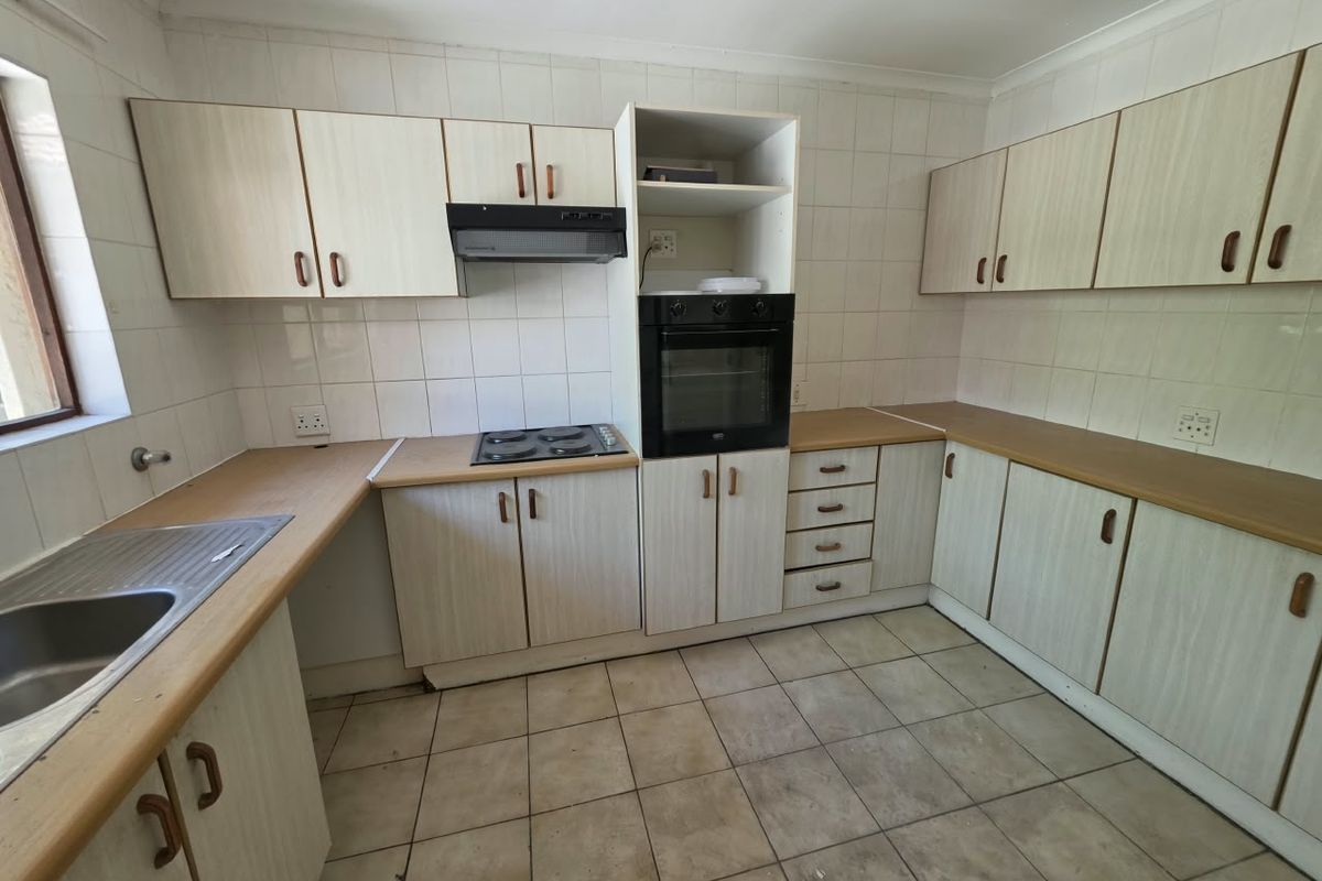 A functional kitchen featuring laminate countertops, built-in oven, electric hob, extractor fan, and ample cabinetry, offering a blank canvas for modern renovation.