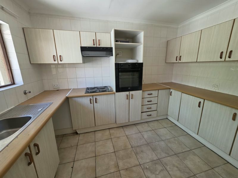 A functional kitchen featuring laminate countertops, built-in oven, electric hob, extractor fan, and ample cabinetry, offering a blank canvas for modern renovation.