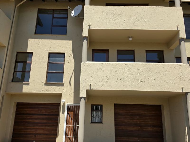 Front elevation of a multi-story townhouse featuring a paved driveway, double garage doors, and two levels of balconies.