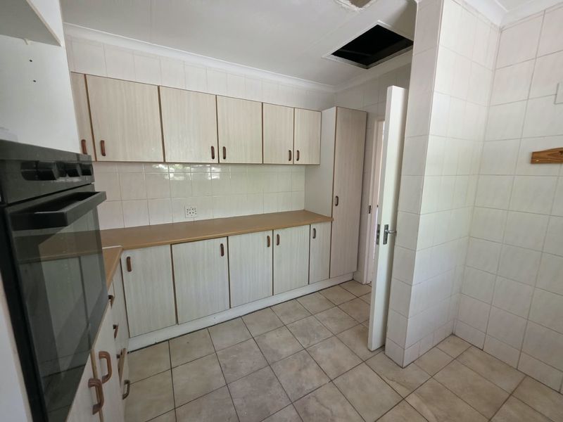 A dated kitchen featuring laminate countertops, tiled backsplash, and built-in cabinetry, currently vacant and requiring maintenance to the ceiling and finishes.