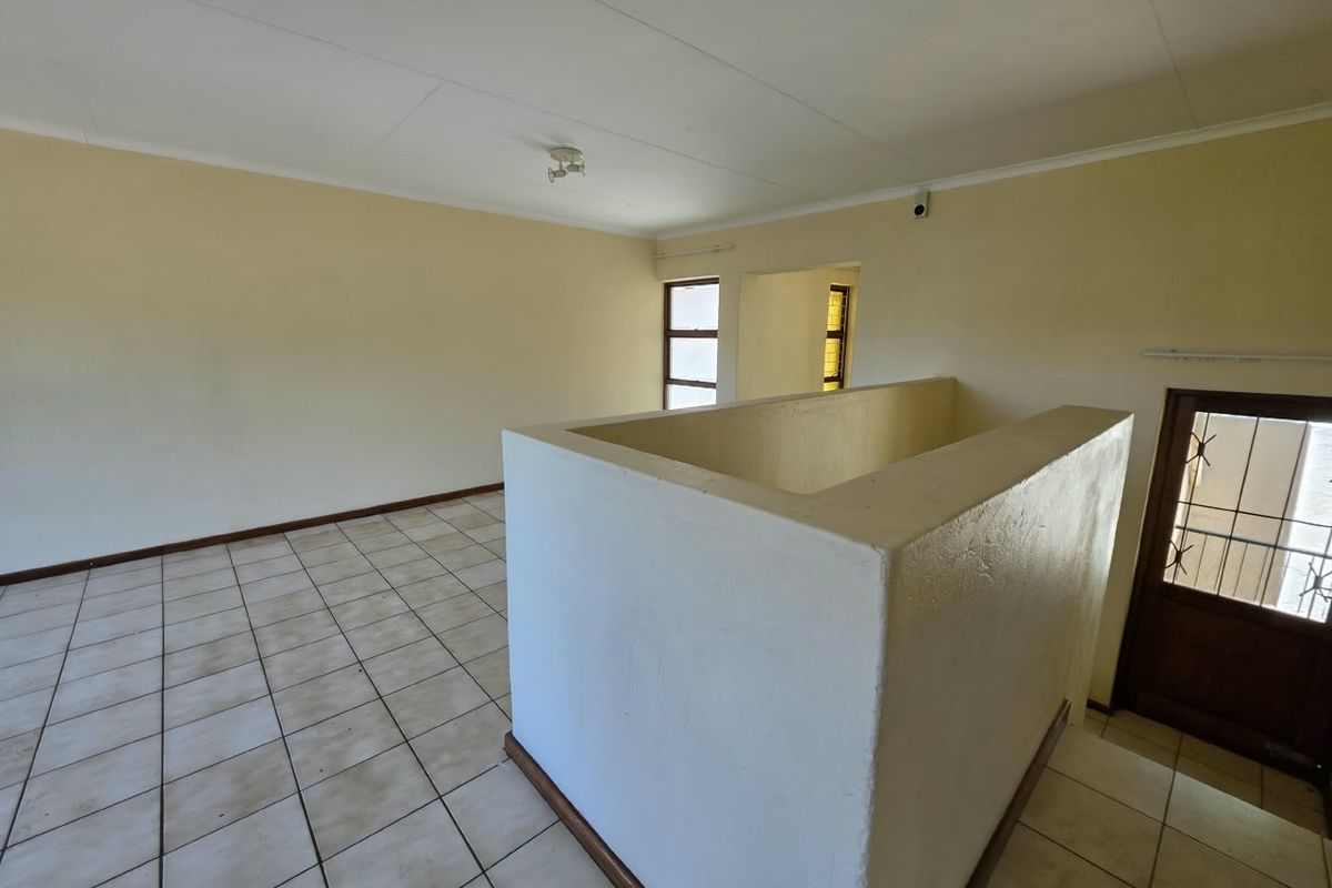 An empty, open-plan living area featuring tiled flooring, a central stairwell balustrade, and neutral wall finishes, ready for personalization.