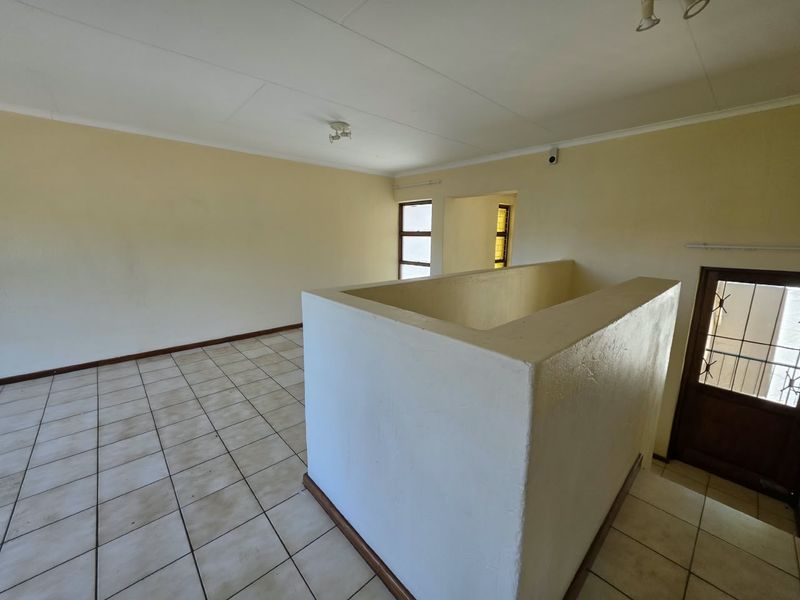 An empty, open-plan living area featuring tiled flooring, a central stairwell balustrade, and neutral wall finishes, ready for personalization.