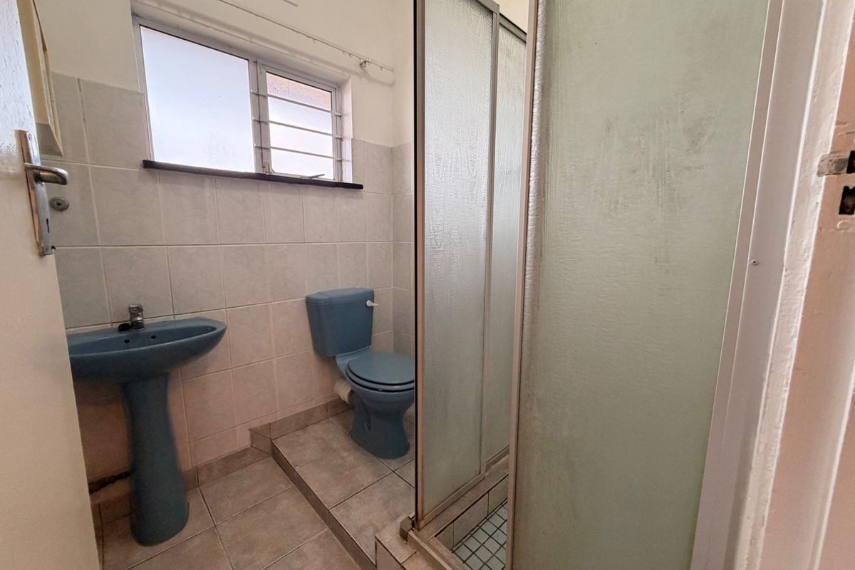 A functional bathroom featuring a pedestal basin, toilet, and a shower enclosure with tiled finishes throughout.