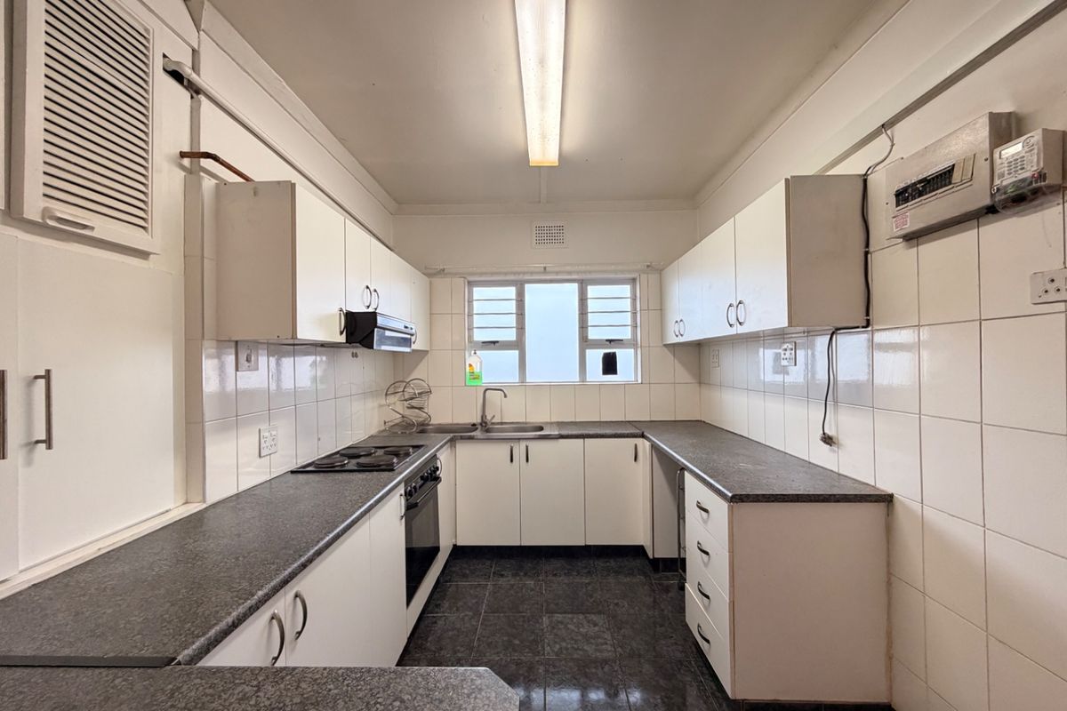 A functional, galley-style kitchen featuring white cabinetry, dark laminate countertops, tiled splashbacks, and built-in cooking appliances, offering a clean and practical workspace.