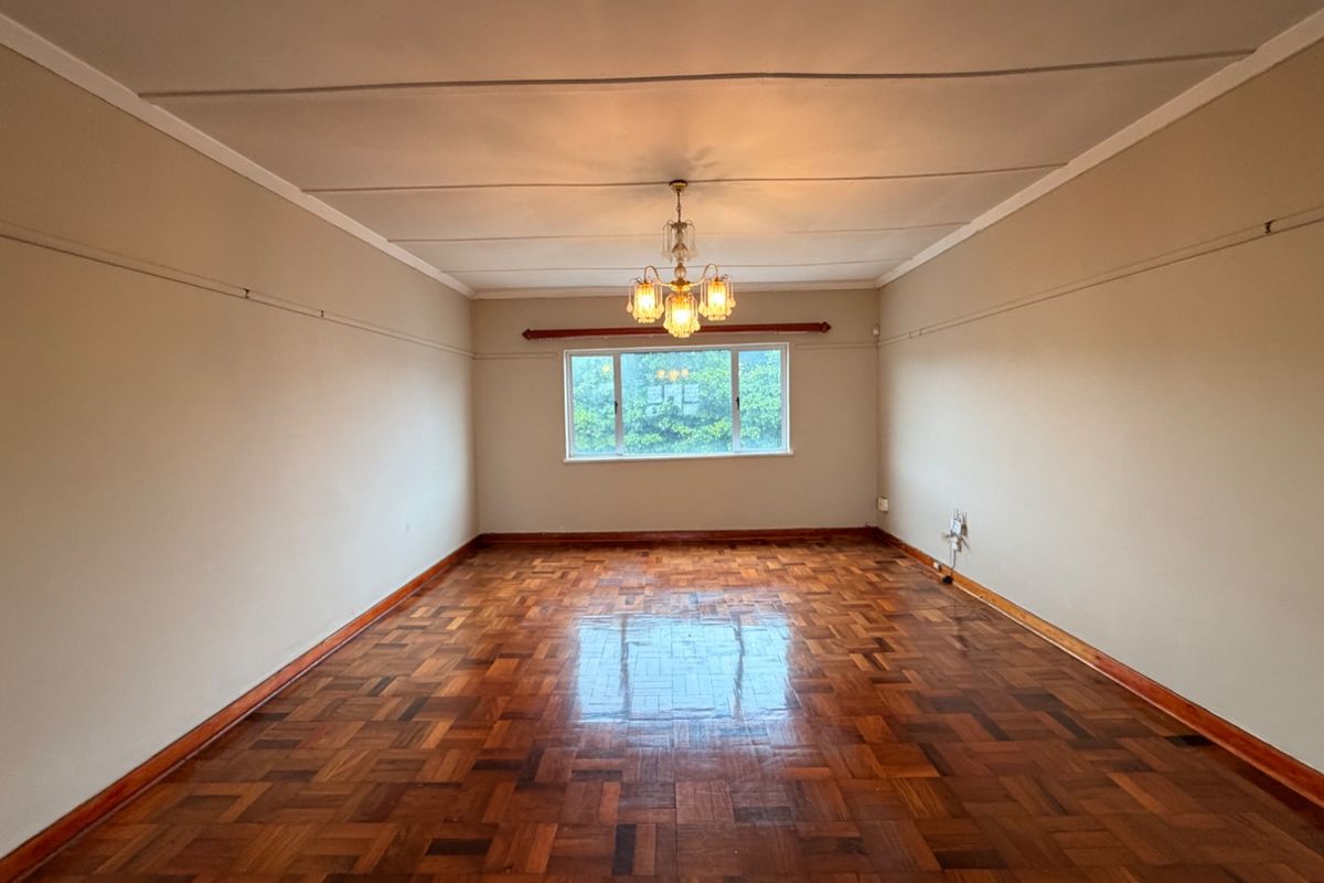 A spacious, empty living room featuring classic parquet flooring, a central chandelier, and neutral walls, offering a blank canvas for interior design.