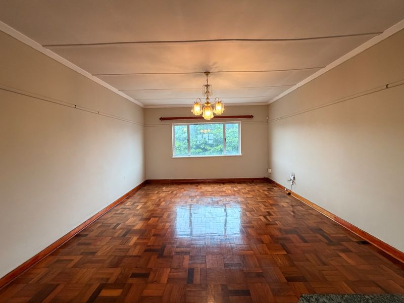 A spacious, empty living room featuring classic parquet flooring, a central chandelier, and neutral walls, offering a blank canvas for interior design.