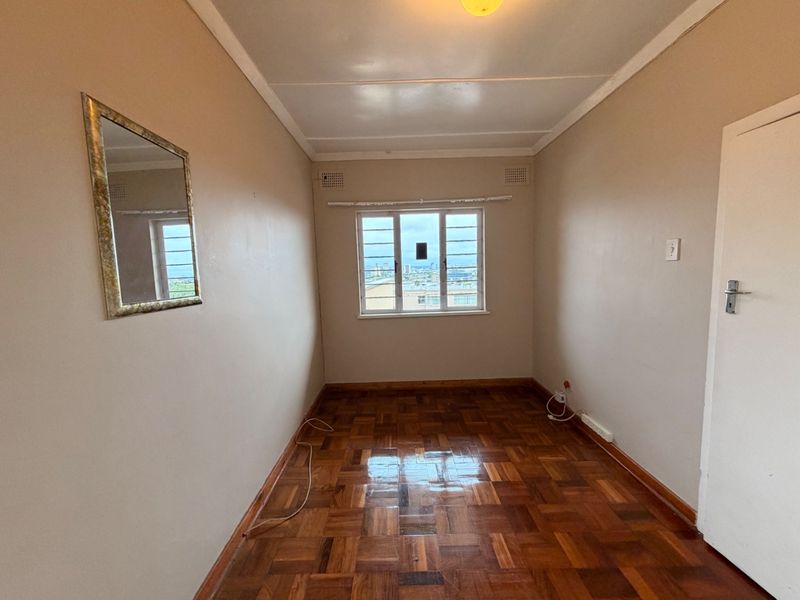 An empty bedroom featuring classic parquet flooring, neutral wall tones, and a metal-framed window with views.