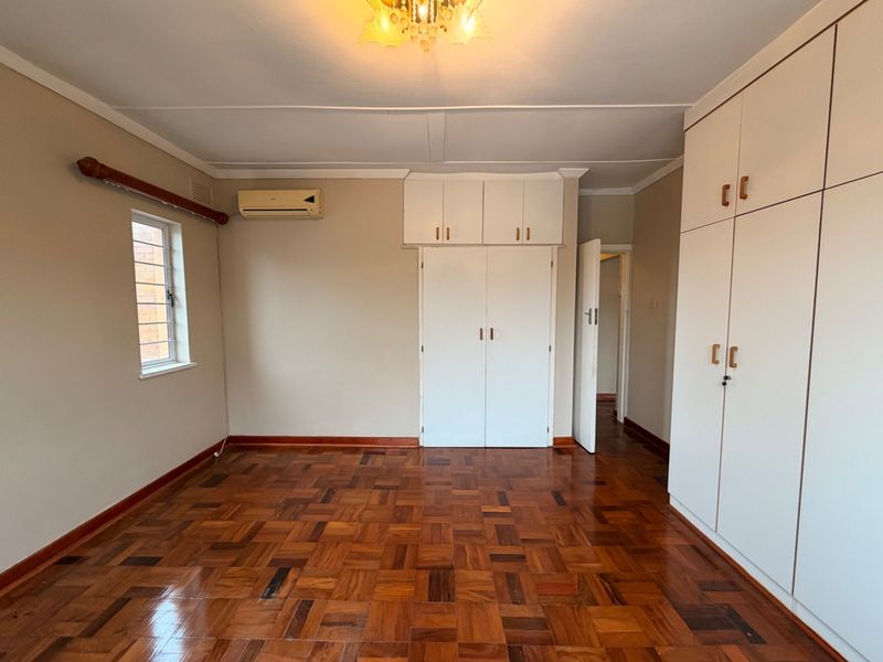 Spacious bedroom featuring polished parquet flooring, extensive built-in cupboard storage, overhead cabinetry, and a wall-mounted air conditioning unit.