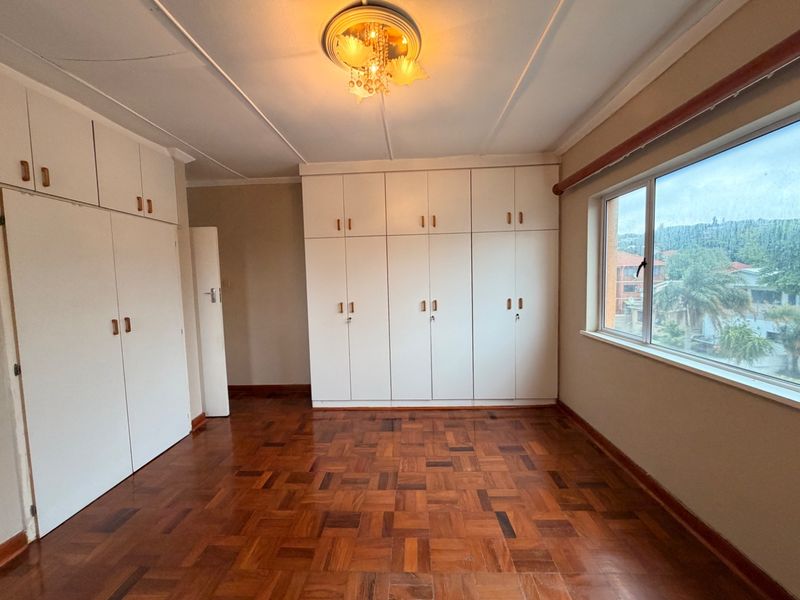 A spacious bedroom featuring classic parquet flooring, extensive built-in cupboard storage, and large windows providing natural light.