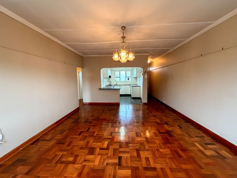 Spacious open-plan living area featuring traditional parquet flooring, a central chandelier, and a functional kitchen pass-through with built-in cabinetry.