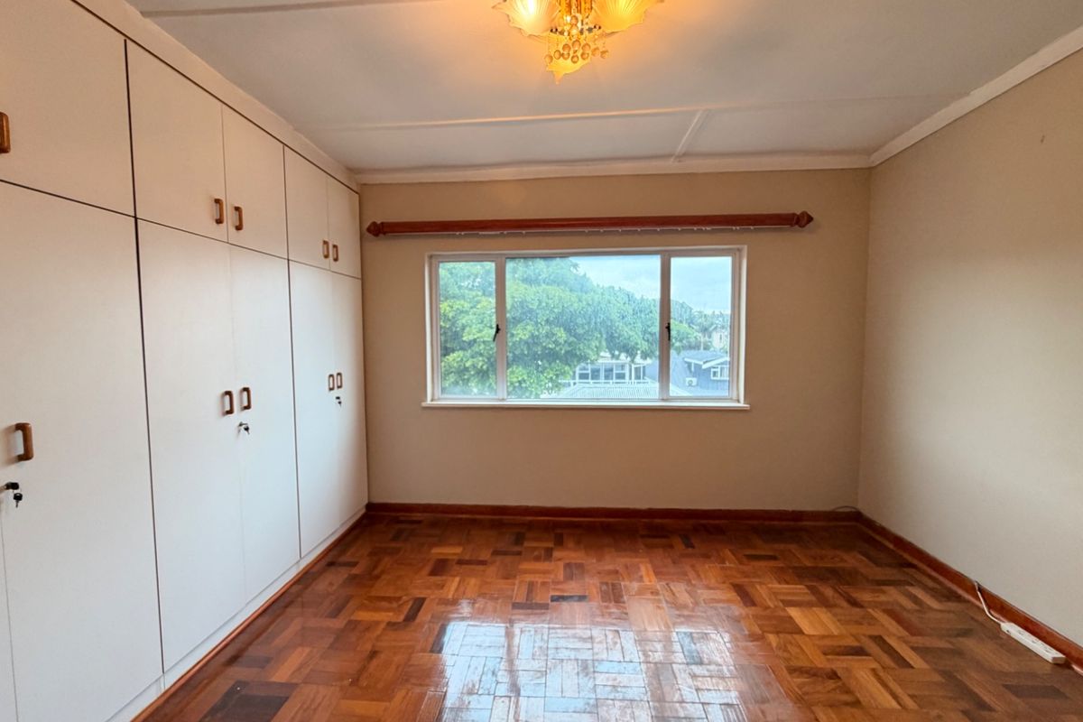 A bright, empty bedroom featuring polished parquet flooring, extensive built-in storage cupboards, and a classic ceiling light fixture.