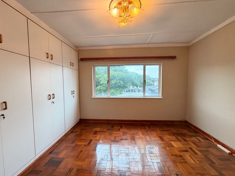 A bright, empty bedroom featuring polished parquet flooring, extensive built-in storage cupboards, and a classic ceiling light fixture.