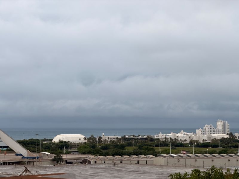 An elevated exterior view overlooking the surrounding coastal landscape, urban infrastructure, and distant ocean horizon under a cloudy sky.