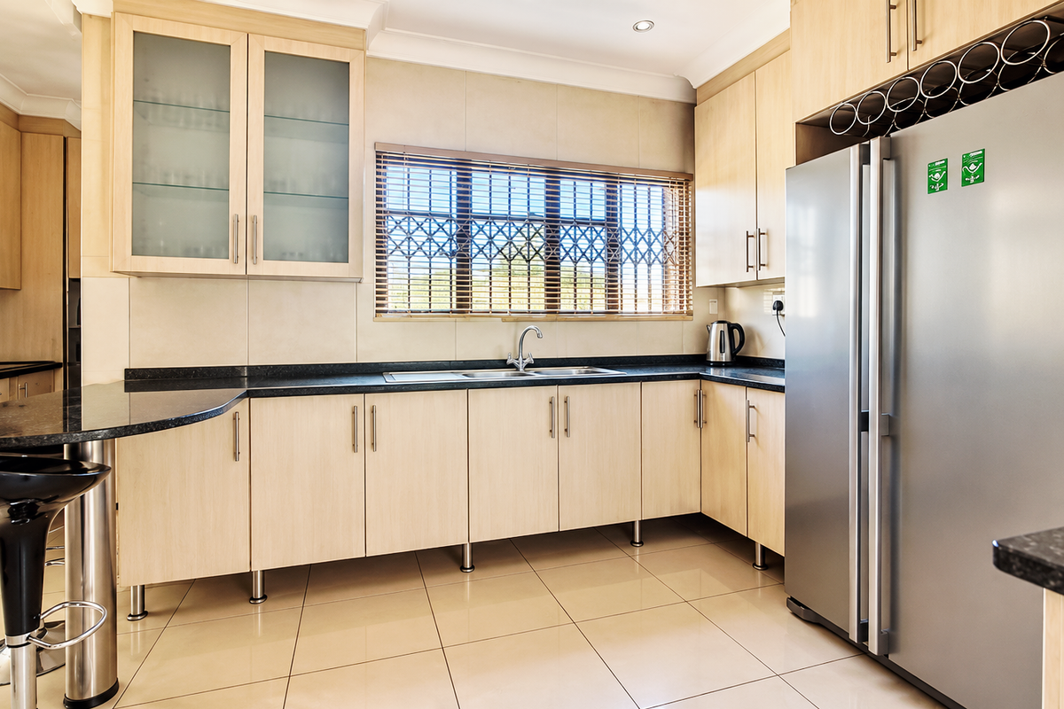 A well-maintained kitchen featuring light wood cabinetry, dark granite countertops, a breakfast bar, and integrated wine storage with tiled flooring.