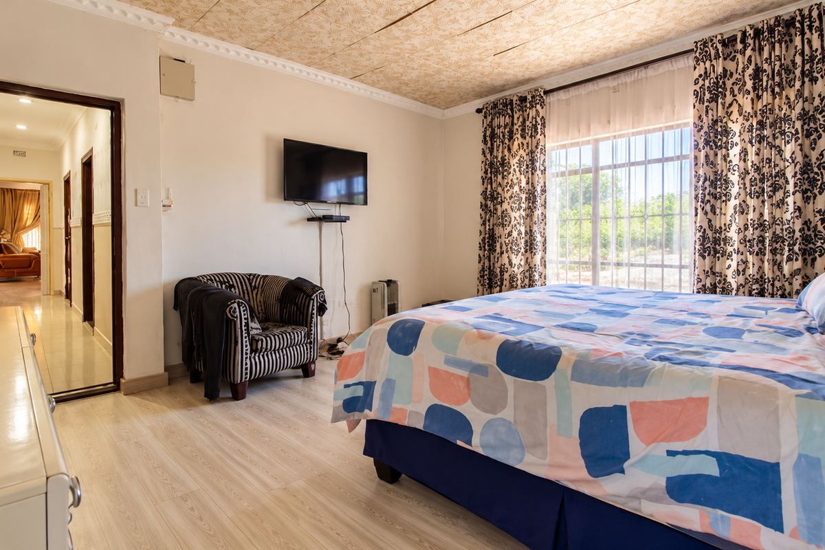 A bedroom featuring laminate flooring, a textured ceiling with decorative cornice, and a window with security bars, providing access to an adjacent hallway.