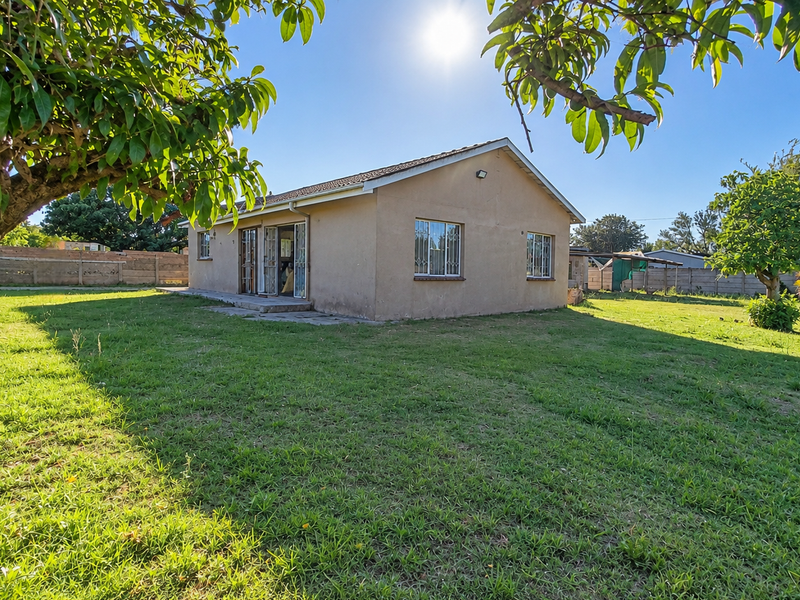 Rear view of the house featuring a spacious garden, concrete patio area, and secure window bars.