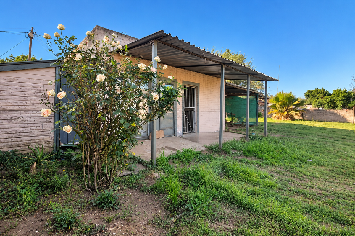 Rear view of the property featuring a covered patio area, brick construction, and a spacious garden with established landscaping.