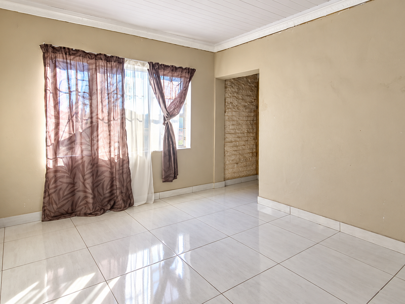 A vacant bedroom featuring polished tiled flooring, a timber ceiling, and an exposed brick accent wall, offering a neutral canvas for personalization.
