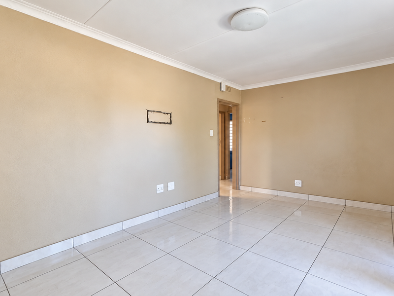 A vacant living room featuring neutral painted walls, tiled flooring, and coved ceiling details, offering a clean canvas for personalization.
