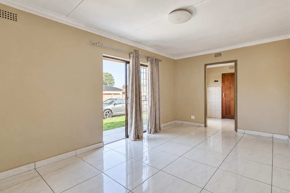 A bright, empty living room featuring neutral walls, polished tiled flooring, and a sliding glass door providing direct access to the outdoor area.