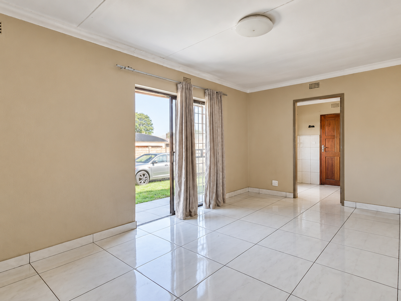 A bright, empty living room featuring neutral walls, polished tiled flooring, and a sliding glass door providing direct access to the outdoor area.