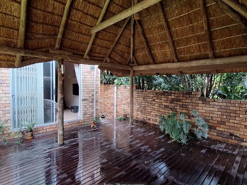 Covered outdoor patio featuring a traditional thatch roof, timber decking, and brick boundary walls, providing a sheltered space for outdoor living.