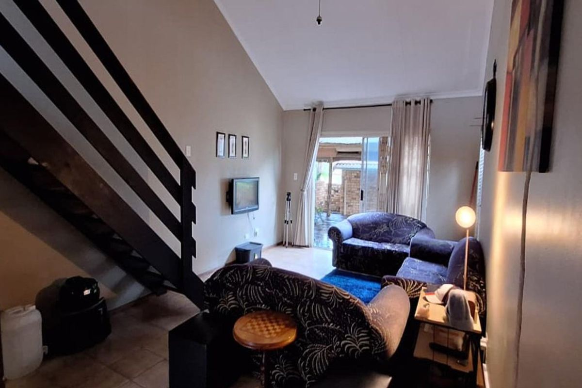 A living room featuring a staircase, vaulted ceiling, and sliding glass door leading to an outdoor area, with tiled flooring throughout.