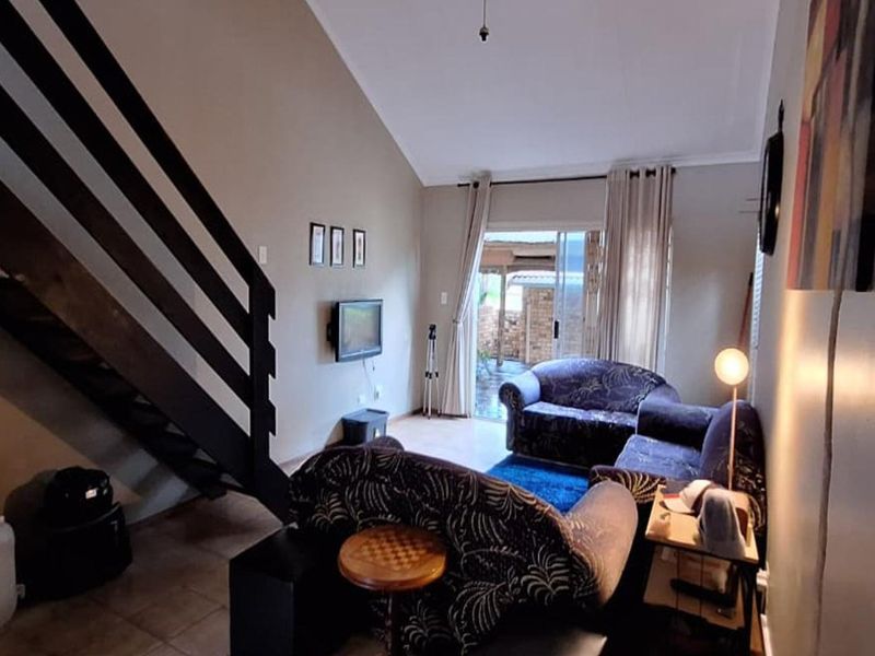 A living room featuring a staircase, vaulted ceiling, and sliding glass door leading to an outdoor area, with tiled flooring throughout.