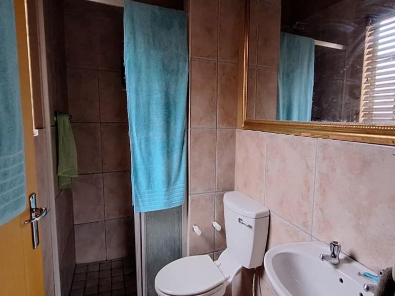 A functional bathroom featuring a shower enclosure, toilet, and pedestal basin with tiled finishes and a large wall-mounted mirror.