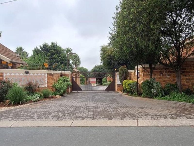 The entrance to the townhouse complex features a secure gated access point with a paved driveway and brick boundary walls.