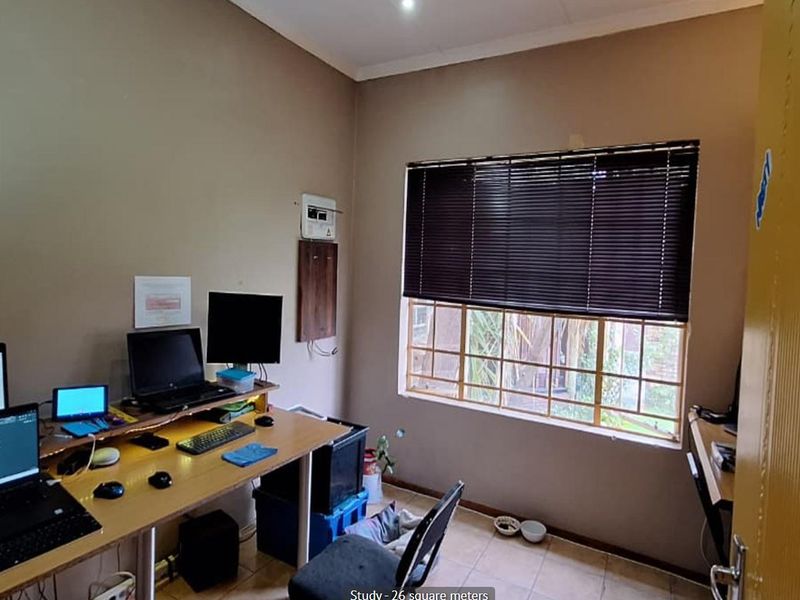 A functional home office space featuring tiled flooring, window security bars, and fitted venetian blinds.
