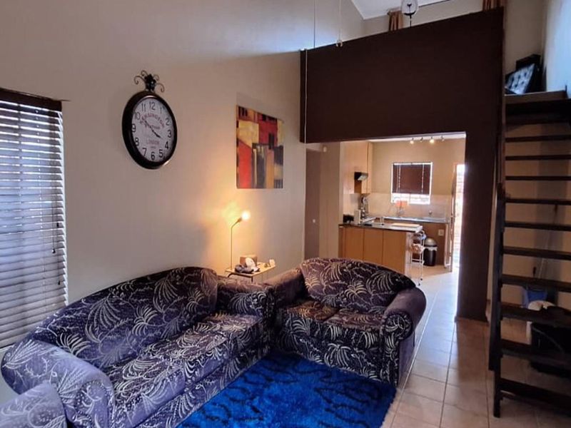 Open-plan living area featuring a staircase leading to a mezzanine level, with an adjoining kitchen space and tiled flooring throughout.