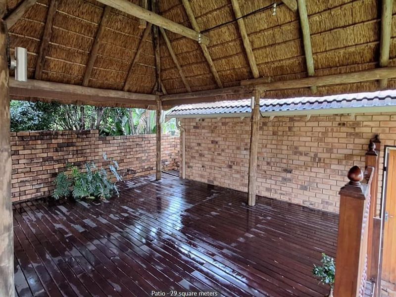 Covered outdoor patio featuring a traditional thatch roof, exposed timber beams, and timber decking, providing a rustic space for outdoor relaxation.