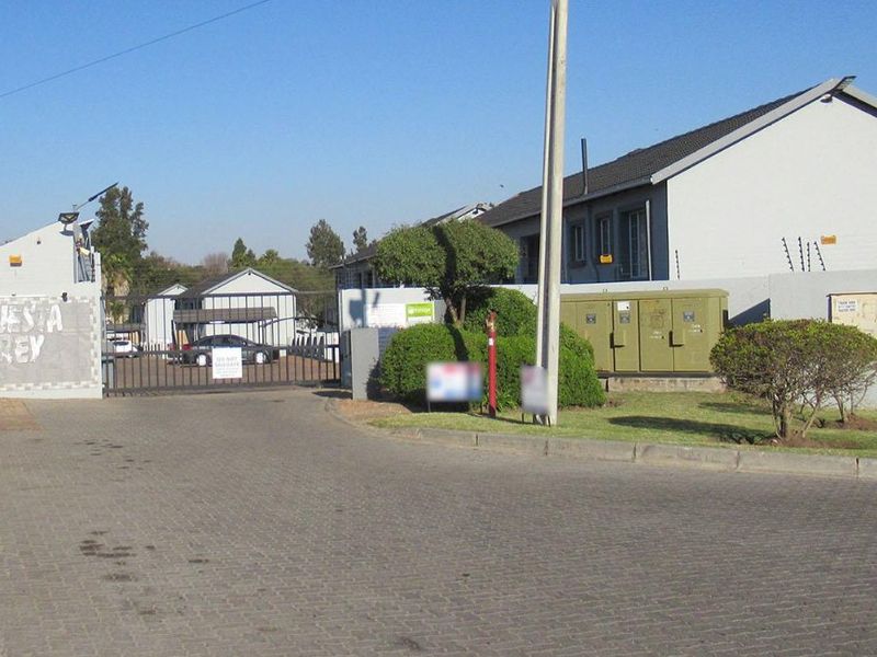 Street view of the residential complex entrance featuring a secure gated access point, perimeter walling with electric fencing, and paved driveway.
