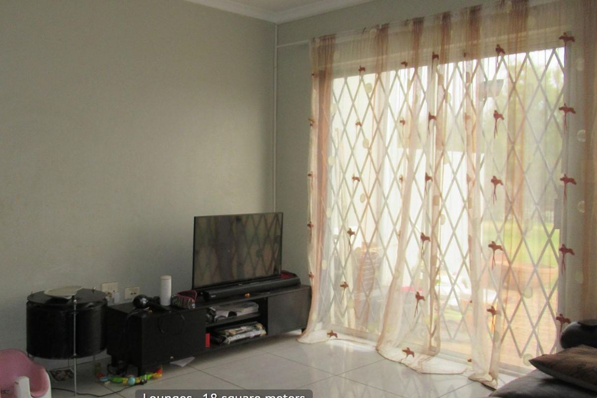 A living room featuring tiled flooring and a sliding glass door with an integrated security gate, providing access to the exterior.