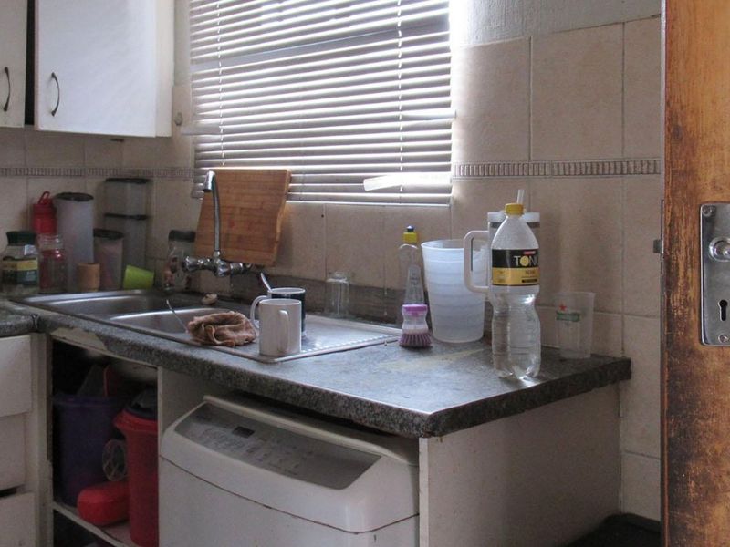 A compact kitchen area featuring a stainless steel sink, tiled backsplash, and built-in cabinetry with laminate countertops.