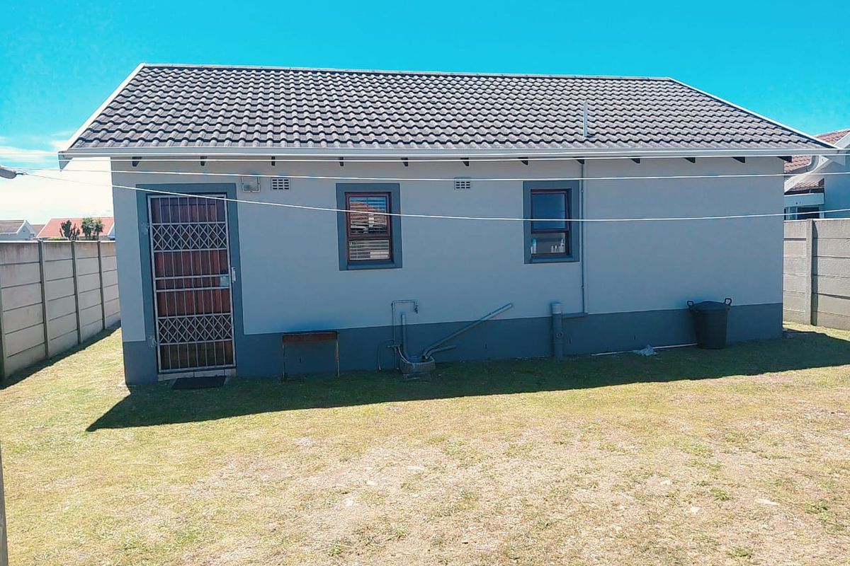 Rear view of the house featuring a tiled roof, security gate, and external plumbing fixtures set against a private garden with boundary walls.
