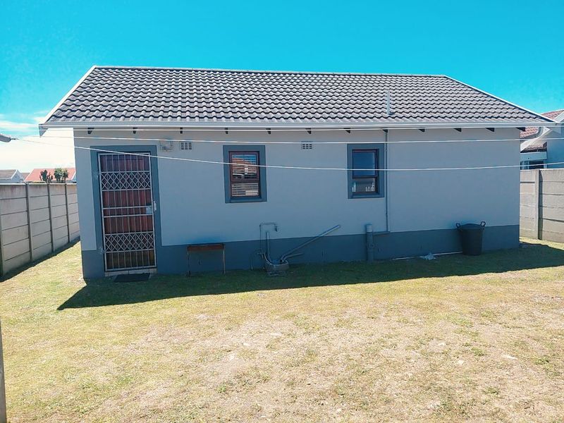 Rear view of the house featuring a tiled roof, security gate, and external plumbing fixtures set against a private garden with boundary walls.