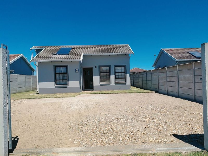Front view of a detached house featuring a tiled roof with solar water heater, gravel driveway, and enclosed by precast concrete boundary walls.