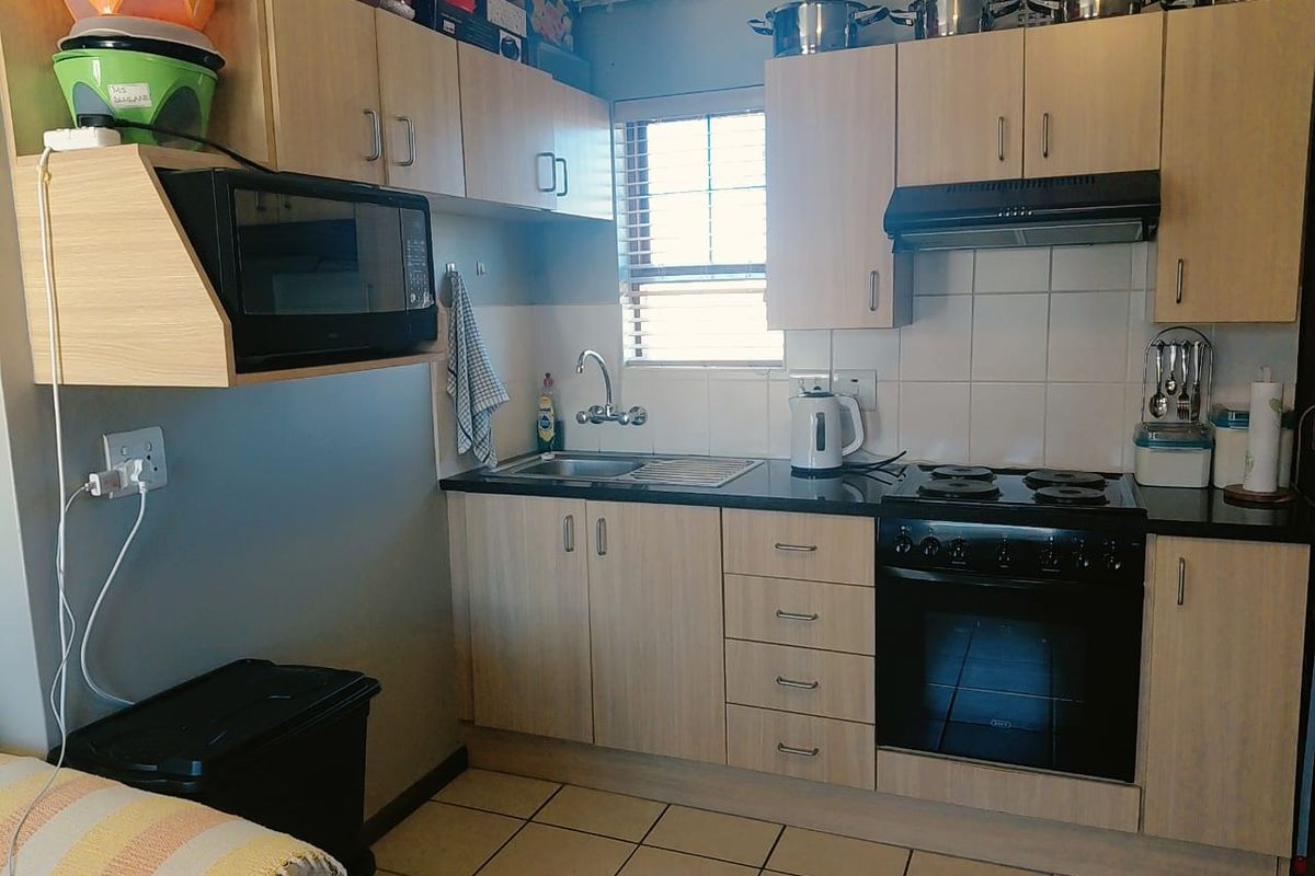Compact kitchen featuring light wood-finish cabinetry, dark countertops, built-in oven with hob, extractor fan, and tiled flooring.