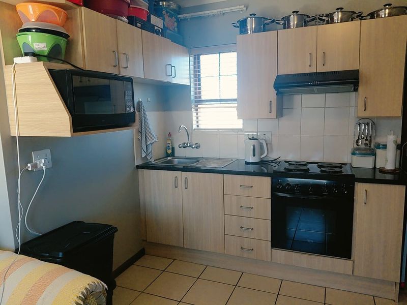 Compact kitchen featuring light wood-finish cabinetry, dark countertops, built-in oven with hob, extractor fan, and tiled flooring.