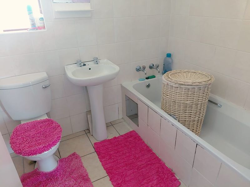 A functional bathroom featuring a pedestal basin, toilet, and bathtub with tiled finishes. The space requires minor maintenance to the bathtub apron.