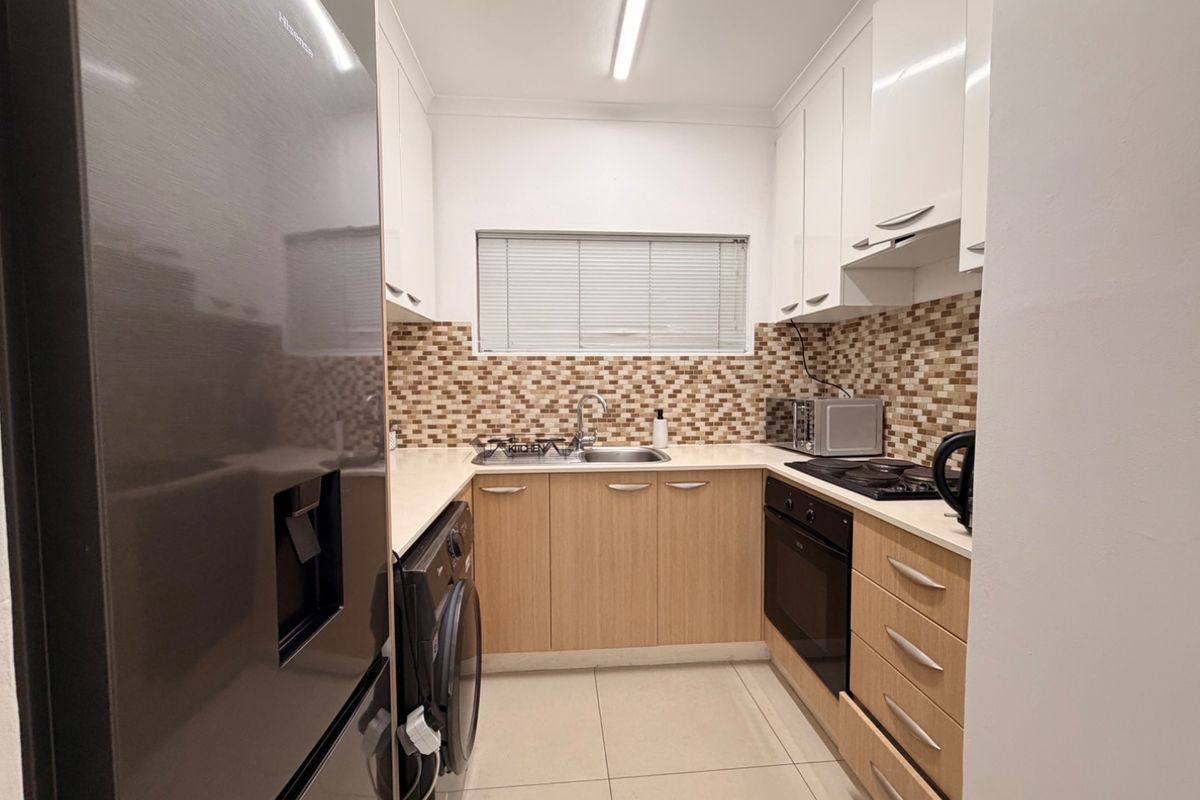 A functional kitchen featuring light wood cabinetry, a mosaic tile backsplash, built-in oven and hob, and tiled flooring.