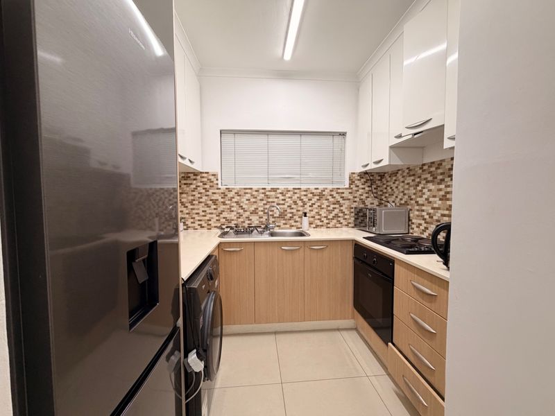 A functional kitchen featuring light wood cabinetry, a mosaic tile backsplash, built-in oven and hob, and tiled flooring.