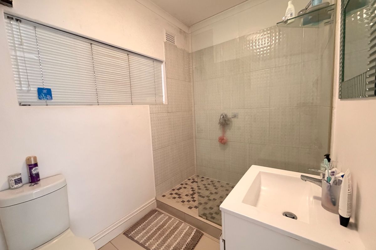 A functional bathroom featuring a walk-in shower with a glass screen, a modern vanity basin, and a toilet, finished with neutral floor tiles.