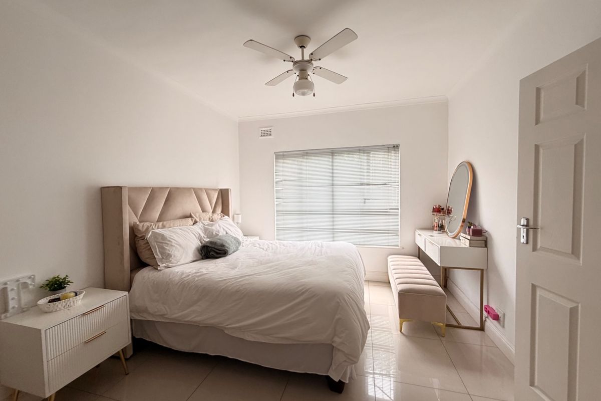 A well-maintained bedroom featuring neutral tiled flooring, a ceiling fan, and venetian blinds, offering a clean and bright living space.