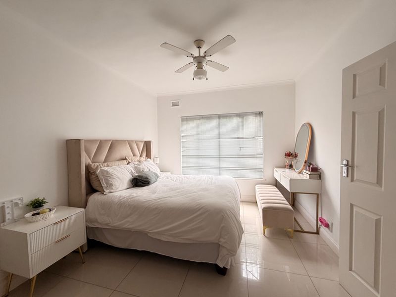 A well-maintained bedroom featuring neutral tiled flooring, a ceiling fan, and venetian blinds, offering a clean and bright living space.