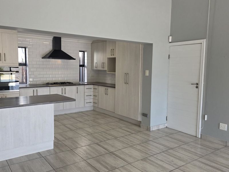 Modern open-plan kitchen featuring light wood cabinetry, subway tile backsplash, built-in oven, gas hob, and a functional kitchen island with tiled flooring throughout.