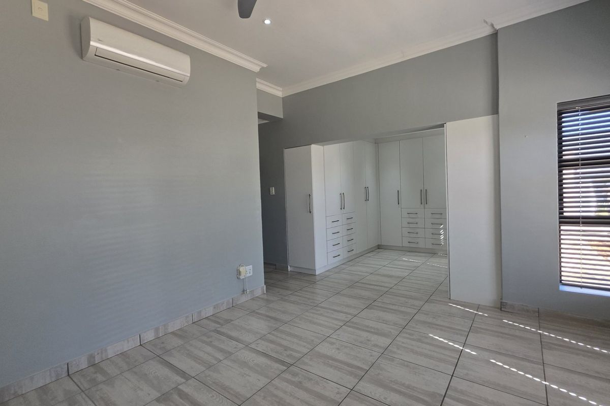 Spacious bedroom featuring neutral grey walls, tiled flooring, built-in cupboards, and a wall-mounted air conditioning unit.